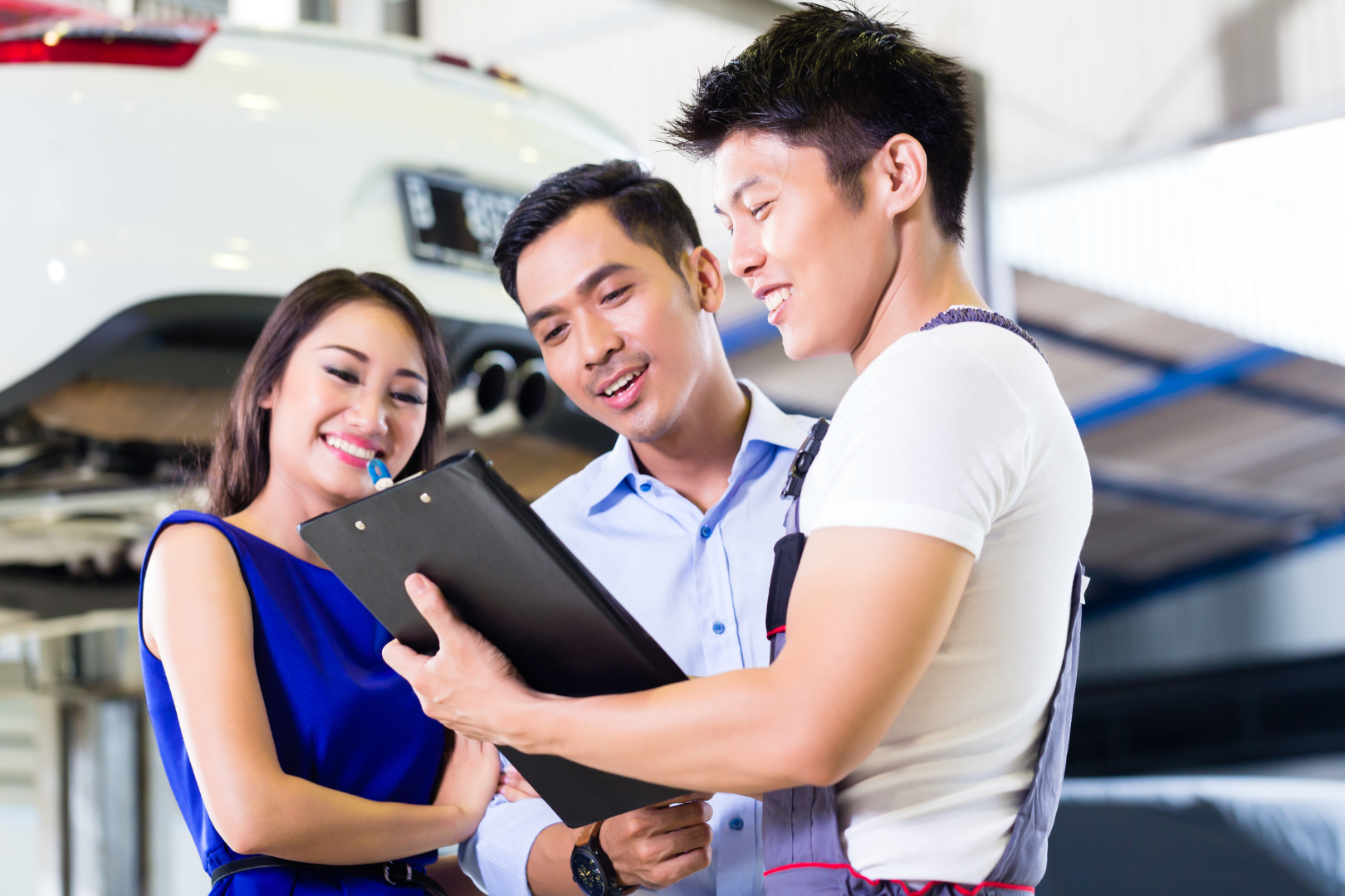Young-couple-at-car-dealership-looking-at-car-repair-bill-with-mechanic