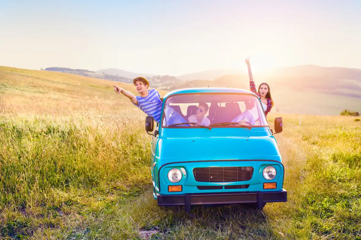 a-turquoise-van-driving-through-golden-fields-with-excited-young-passengers-leaning-out-windows-during-sunset